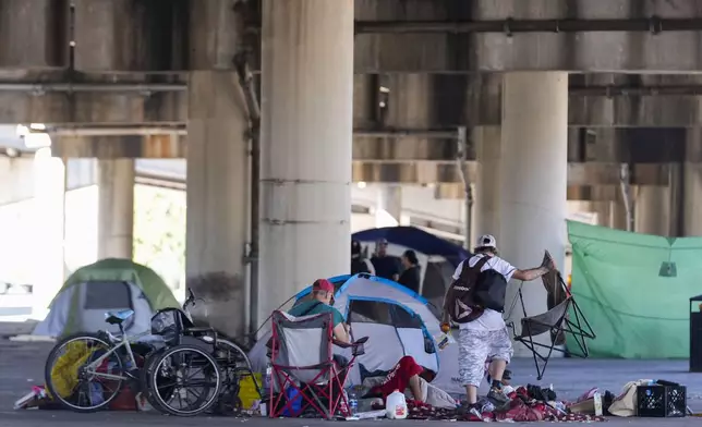 People living in a homeless encampment pick up belongings after Louisiana State police gave instructions for them to move to a different pre-designated location as they perform a sweep in advance of a Taylor Swift concert in New Orleans, Wednesday, Oct. 23, 2024. (AP Photo/Gerald Herbert)