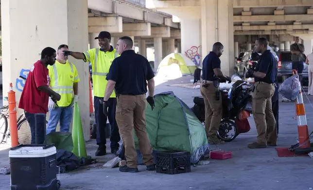 Louisiana State police give instructions to people living in a homeless encampment to move to a different pre-designated location as they perform a sweep in advance of a Taylor Swift concert in New Orleans, Wednesday, Oct. 23, 2024. (AP Photo/Gerald Herbert)