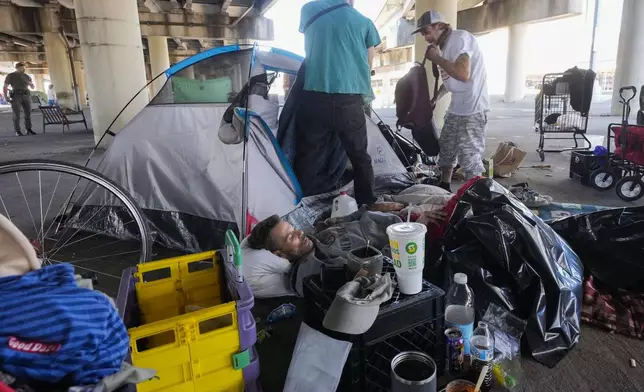 People living in a homeless encampment pick up belongings after Louisiana State police gave instructions for them to move to a different pre-designated location as they perform a sweep in advance of a Taylor Swift concert in New Orleans, Wednesday, Oct. 23, 2024. (AP Photo/Gerald Herbert)