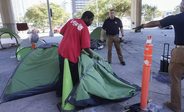 Louisiana State police give instructions to people living in a homeless encampment to move to a different pre-designated location as they perform a sweep in advance of a Taylor Swift concert in New Orleans, Wednesday, Oct. 23, 2024. (AP Photo/Gerald Herbert)