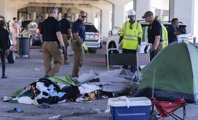 Louisiana State police give instructions to people living in a homeless encampment to move to a different pre-designated location as they perform a sweep in advance of a Taylor Swift concert in New Orleans, Wednesday, Oct. 23, 2024. (AP Photo/Gerald Herbert)