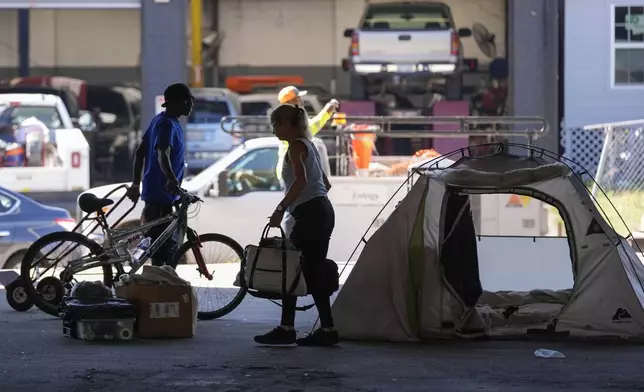 People living in a homeless encampment pick up belongings after Louisiana State police gave instructions for them to move to a different pre-designated location as they perform a sweep in advance of a Taylor Swift concert in New Orleans, Wednesday, Oct. 23, 2024. (AP Photo/Gerald Herbert)