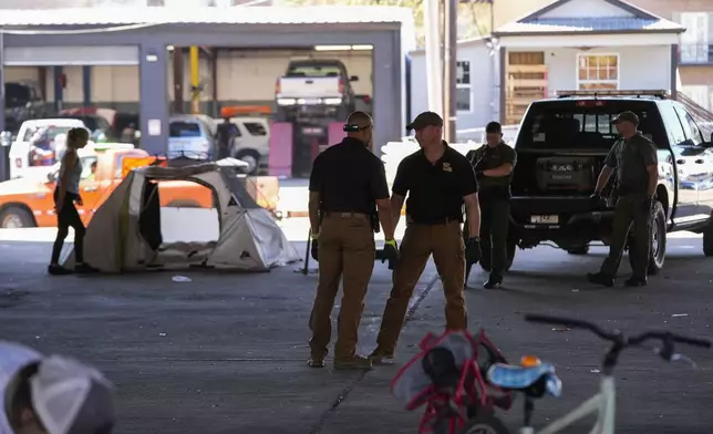 Louisiana State police give instructions to people living in a homeless encampment to move to a different pre-designated location as they perform a sweep in advance of a Taylor Swift concert in New Orleans, Wednesday, Oct. 23, 2024. (AP Photo/Gerald Herbert)