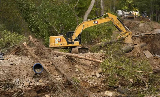 A backhoe is used to clear debris left by Hurricane Helene that washed away a road and destroyed a waterline for the city of Asheville Wednesday, Oct. 2, 2024, in Black Mountain, N.C. (AP Photo/Jeff Roberson)