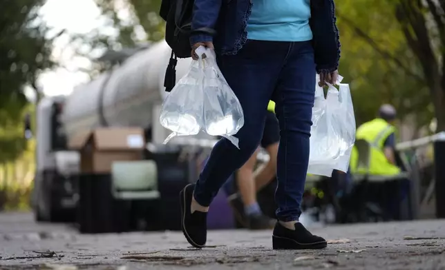 A person carries bags of fresh water after filling up from a tanker at a distribution site in the aftermath of Hurricane Helene Wednesday, Oct. 2, 2024, in Asheville, N.C. (AP Photo/Jeff Roberson)