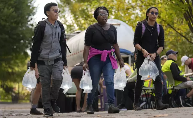 People carry bags of fresh water after filling up at a distribution site in the aftermath of Hurricane Helene Wednesday, Oct. 2, 2024, in Asheville, N.C. (AP Photo/Jeff Roberson)