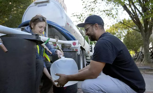 Reginald Klemz, right, fills a container of fresh water from a tanker with the help of volunteer Julie Koenke in the aftermath of Hurricane Helene Wednesday, Oct. 2, 2024, in Asheville, N.C. (AP Photo/Jeff Roberson)