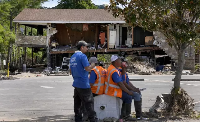 Workers helping with clean up efforts stop for lunch under the shade of a tree as a building destroyed by Hurricane Helene is seen in the background Saturday, Oct. 5, 2024, in Newport, Tenn. (AP Photo/Jeff Roberson)