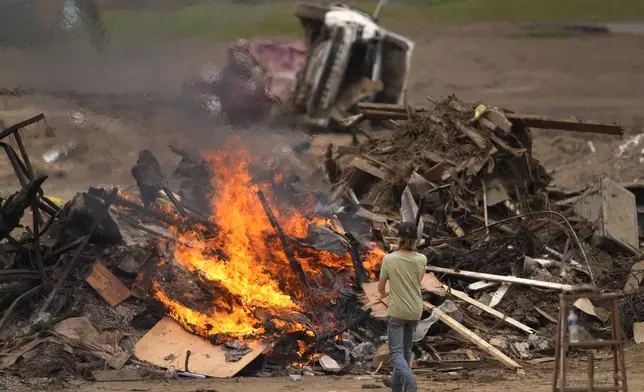 A person throws objects on a burning debris pile in the aftermath of Hurricane Helene, Friday, Oct. 4, 2024, in Erwin, Tenn. (AP Photo/Jeff Roberson)