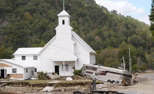 Dominick Gucciardo walks to his home past a bus pushed by flood waters rests against Laurel Branch Baptist church in the aftermath of Hurricane Helene, Thursday, Oct. 3, 2024, in Pensacola, N.C. (AP Photo/Mike Stewart)