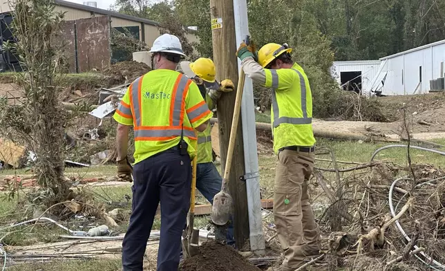 Contractors for Duke Energy dig a hole by hand to replace a utility pole in an area of destroyed electrical lines near the Swannanoa River in Asheville, N.C., on Friday, Oct. 4, 2024. (AP Photo/Jeff Amy)