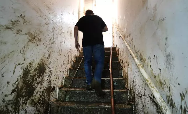 Contractor Joshua Taylor walks up stairs covered in mud leading to the basement of a funeral home that was flooded in the aftermath of Hurricane Helene while working to clean up the building Saturday, Oct. 5, 2024, in Newport, Tenn. (AP Photo/Jeff Roberson)