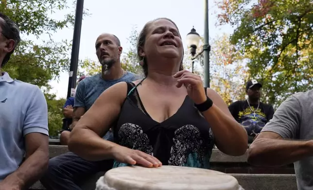 A woman plays music at a drum circle Friday, Oct. 4, 2024 in Asheville, N.C., a week after Hurricane Helene upended lives across the Southeast. (AP Photo/Brittany Peterson)