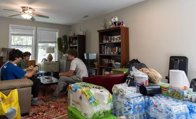 Cases of water, canned food and other supplies are seen in the living room while high school senior Ari Cohen, right, and his friends play a game of Uno, Friday, Oct. 18, 2024, in Asheville, N.C. (AP Photo/Stephanie Scarbrough)