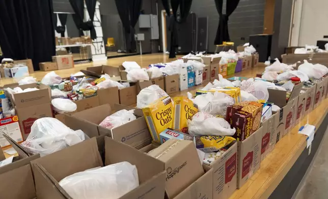 Boxes of food items line the stage in an auditorium of the Dr. Wesley Grant Sr. Southside Community Center in Asheville, N.C., where high school senior Nathan Flaherty volunteers in the aftermath of Hurricane Helene, Wednesday, Oct. 16, 2024. (AP Photo/Stephanie Scarbrough)