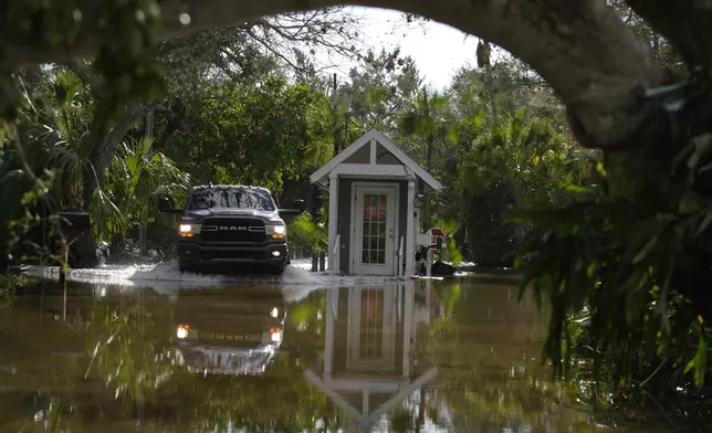 A pick up drives past a guard gate on a flooded street in Siesta Key, Fla., following the passage Hurricane Milton, Thursday, Oct. 10, 2024. (AP Photo/Rebecca Blackwell)