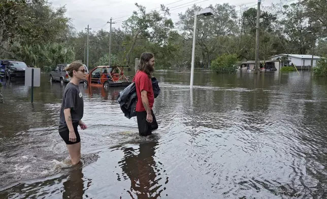 Kaylee Swanson, left, and Connor Hughes walk through floodwaters from the Alafia river caused by Hurricane Milton Friday, Oct. 11, 2024, in Lithia, Fla. (AP Photo/Chris O'Meara)