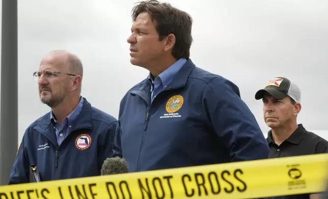 Florida Gov. Ron DeSantis, center, Kevin Guthrie, left, Executive Director of the Florida Division of Emergency Management and Fla. Rep. Toby Overdorf take questions during a news conference in front of a St. Lucie County Sheriff's parking facility that was damaged by a tornado spawned ahead of Hurricane Milton destroyed it, Thursday, Oct. 10, 2024, in Fort Pierce. (AP Photo/Wilfredo Lee)