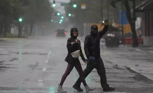 People walk through nearly-deserted downtown Tampa, Fla., in windy and rainy conditions during the approach of Hurricane Milton, Wednesday, Oct. 9, 2024. (AP Photo/Rebecca Blackwell)