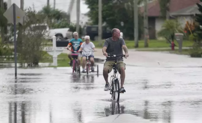 FILE - Cyclists ride through flooded streets in a neighborhood damaged by tornados spawned ahead of Hurricane Milton, Oct. 10, 2024, in Fort Pierce, Fla. (AP Photo/Wilfredo Lee, File)