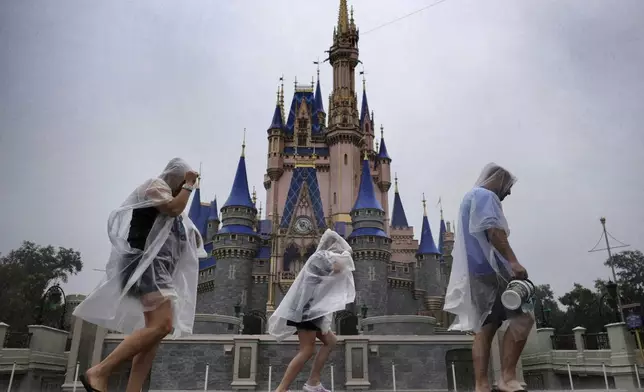 Guests weather early bands of rain from Hurricane Milton at the Magic Kingdom at Walt Disney World in Bay Lake, Fla., Wednesday, Oct. 9, 2024. All four of Disney's Florida theme parks closed early Wednesday due to the forecast track of the storm. (Joe Burbank/Orlando Sentinel via AP)