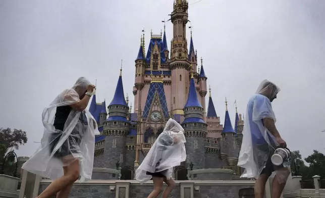 Guests weather early bands of rain from Hurricane Milton at the Magic Kingdom at Walt Disney World in Bay Lake, Fla., Wednesday, Oct. 9, 2024. All four of Disney's Florida theme parks closed early Wednesday due to the forecast track of the storm. (Joe Burbank/Orlando Sentinel via AP)