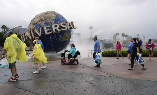 Tourists walk along Universal Orlando Resort city walk before the park closed early for the arrival of Hurricane Milton, Wednesday, Oct. 9, 2024, in Orlando, Fla. (AP Photo/John Raoux)