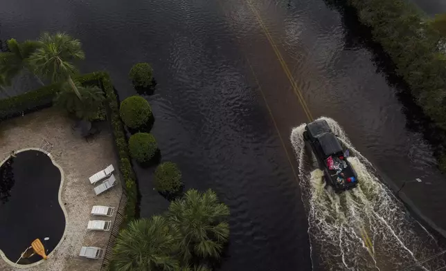 People ride in the back of a pickup avoiding floodwaters in the Tarpon Woods neighborhood of Palm Harbor, Fla., following Hurricane Milton, Friday, Oct. 11, 2024. (AP Photo/Julio Cortez)