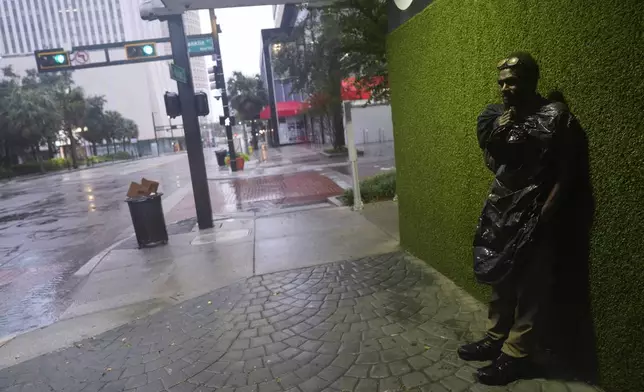 Melvin Lee HIcks, who is homeless, wears a trash bag to protect against wind-driven rain, as he stands on a street in downtown Tampa, Fla., during the approach of Hurricane Milton, Wednesday, Oct. 9, 2024. (AP Photo/Rebecca Blackwell)