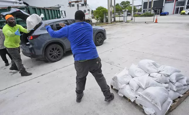 North Miami Beach, Fla., public service workers Roshad Smiley, left, and Mikhail Pollar, foreground, load sandbags to help prevent flooding, to residents cars as Hurricane Milton prepares to strike Florida, Tuesday, Oct. 8, 2024, in North Miami Beach. (AP Photo/Wilfredo Lee)