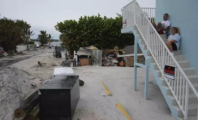 Andy Malloy, top, whose family has owned the home next door for more than 50 years, rests on the steps of Sunset Villa Condos with his wife Kim, as they take some time to say goodbye before heeding evacuation orders ahead of the arrival of Hurricane Milton, in Bradenton Beach, Fla., on Anna Maria Island, Tuesday, Oct. 8, 2024. (AP Photo/Rebecca Blackwell)