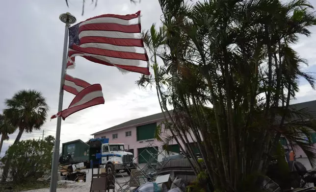 A tattered American flag flaps outside a home as crews work to clean up piles of debris from Hurricane Helene flooding ahead of the arrival of Hurricane Milton, in Holmes Beach on Anna Maria Island, Fla., Tuesday, Oct. 8, 2024. (AP Photo/Rebecca Blackwell)