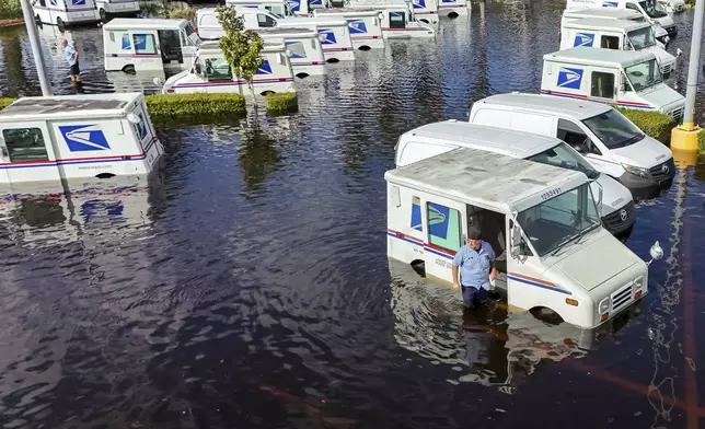 A USPS worker inspects trucks that had been relocated to protect them from wind but which are now underwater as intense rain from Hurricane Milton caused the Anclote River to flood, Friday, Oct. 11, 2024, in New Port Richey, Fla. (AP Photo/Mike Carlson)