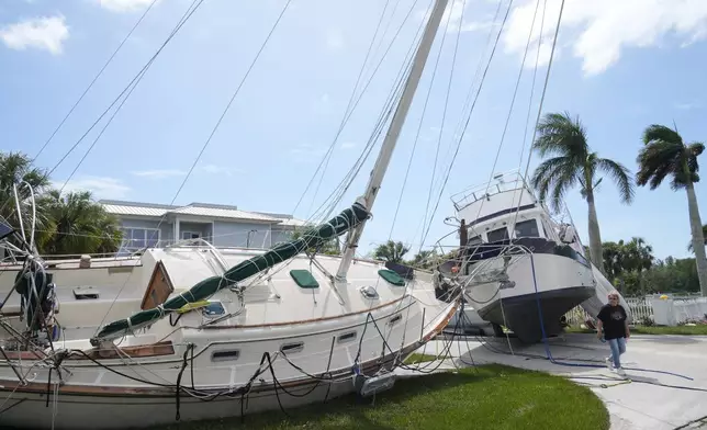 Su Miscia walks between two large boats that broke their moorings during Hurricane Milton and ended on on a street, Thursday, Oct. 10, 2024, in Punta Gorda, Fla. (AP Photo/Marta Lavandier)