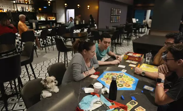 The Segundo family, who evacuated from nearby Davis Island, plays a board game with their dog Cassie looking on, as Hurricane Milton makes landfall on Florida's Gulf Coast, at Hyatt Place Tampa Downtown hotel in Tampa, Fla., Wednesday, Oct. 9, 2024. (AP Photo/Rebecca Blackwell)