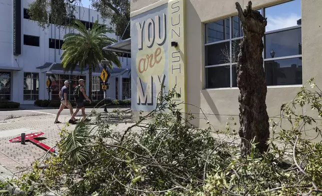 Residents walk past trees and signs damaged by winds from Hurricane Milton on Thursday, Oct. 10, 2024, in St. Petersburg, Fla. (AP Photo/Mike Carlson)