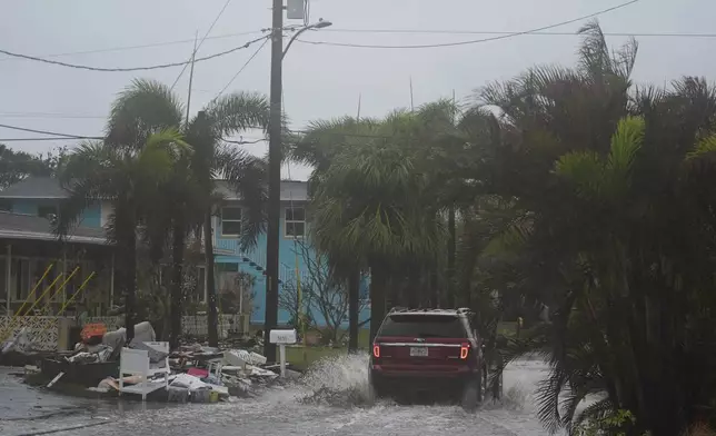 A car drives past a pile of debris from Hurricane Helene flooding, along a street that had already begun flooding from rain ahead of the arrival of Hurricane Milton, in Gulfport, Fla., Wednesday, Oct. 9, 2024. (AP Photo/Rebecca Blackwell)