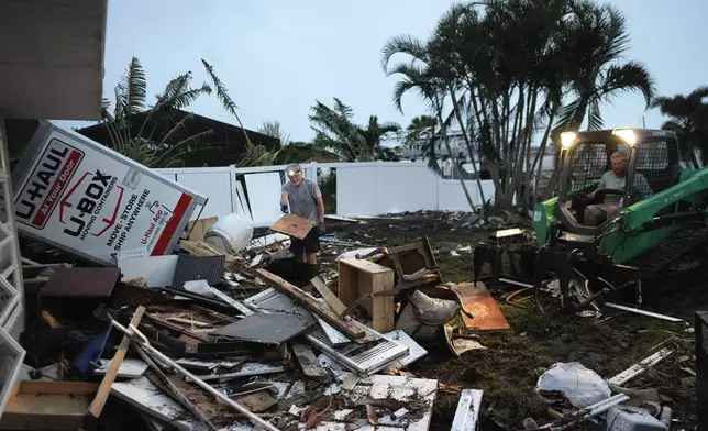 Homeowner Robert Turick, 68, left, and storm waste removal contractor Sven Barnes work to clear debris that Hurricane Milton storm surge swept from other properties into Turick's canal-facing back yard, in Englewood, Fla., Friday, Oct. 11, 2024. Turick, whose family has owned the home for more than 25 years, said it had never flooded until 2022's Hurricane Ian, but since then, it has flooded in three more hurricanes, each bringing higher water levels than the last. (AP Photo/Rebecca Blackwell)