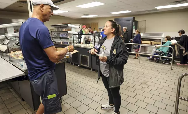 Pasco Schools administrator Jill Cortier speaks with Muhamed Aftah during a meal service at a hurricane shelter at River Ridge Middle/High School in preparation for Hurricane Milton, Wednesday, Oct. 9, 2024, in New Port Richey, Fla. (AP Photo/Mike Carlson)