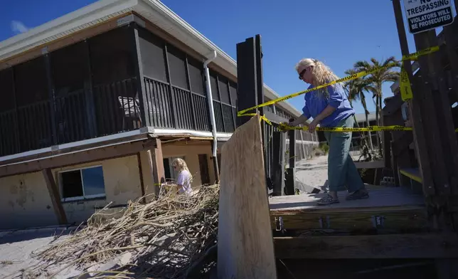 Theresa Carrithers, property manager of Sea Oats Beach Club, puts up caution tape around the hotel's damaged infrastructure, following the passage of Hurricane Milton, on Manasota Key in Englewood, Fla.,, Sunday, Oct. 13, 2024. (AP Photo/Rebecca Blackwell)