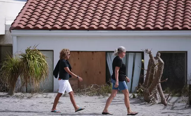 Area residents walk past a beachfront home with sand reaches half-way up its sliding doors, as they survey Hurricane Milton damage, on the island of Venice, Fla., Friday, Oct. 11, 2024. (AP Photo/Rebecca Blackwell)