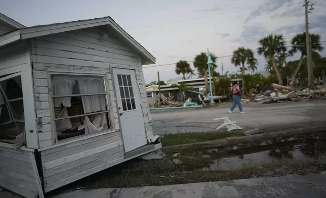 A woman, right, walks past a home that was swept partially into the road during the passage of Hurricane Milton, on Manasota Key, Fla., Saturday, Oct. 12, 2024. (AP Photo/Rebecca Blackwell)