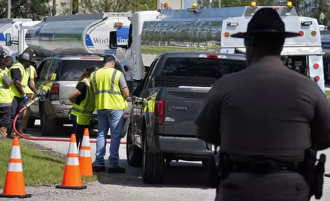 A Florida Highway Patrol officer watches as fuel depot workers distribute gas to residents Saturday, Oct. 12, 2024, in Plant City, Fla. Gas stations are slow to reopen after the effects of Hurricane Milton. (AP Photo/Chris O'Meara)