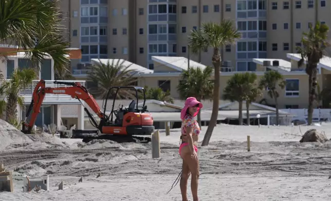 A condominium owner who says her unit, at the back of the property, was luckily undamaged, walks beside an almost-buried fence as she surveys the beginning of work to remove feet worth of extra sand from the beach and beachfront properties, in Venice, Fla.,following the passage of Hurricane Milton, Saturday, Oct. 12, 2024. (AP Photo/Rebecca Blackwell)