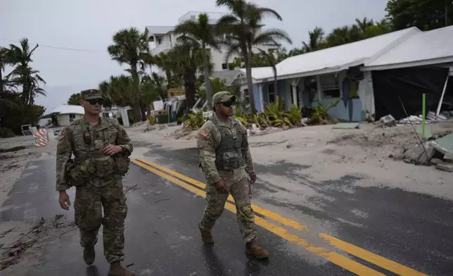 Members of the Florida Army National Guard walk past a home slated for demolition after being damaged in Hurricane Helene, as they check for any remaining residents, ahead of the arrival of Hurricane Milton, Tuesday, Oct. 8, 2024, on Anna Maria Island, Fla. (AP Photo/Rebecca Blackwell)