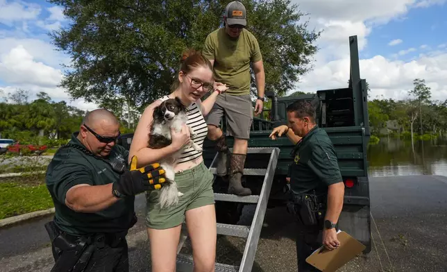 Sarah McRee holds a dog named Poe as she is helped off a high-clearance vehicle by Panellas County Sheriff officials after she was escorted in and out of the Tarpon Woods neighborhood as people return to their homes following Hurricane Milton, Friday, Oct. 11, 2024, in Palm Harbor, Fla. (AP Photo/Julio Cortez)