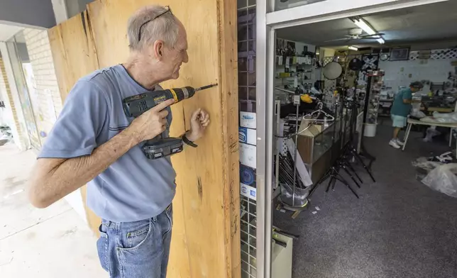 Jim Smetzer puts up boards as his wife Annette clears merchandise from their camera store in preparation for Hurricane Milton on Tuesday, Oct. 8, 2024, in New Port Richey, Fla. (AP Photo/Mike Carlson)