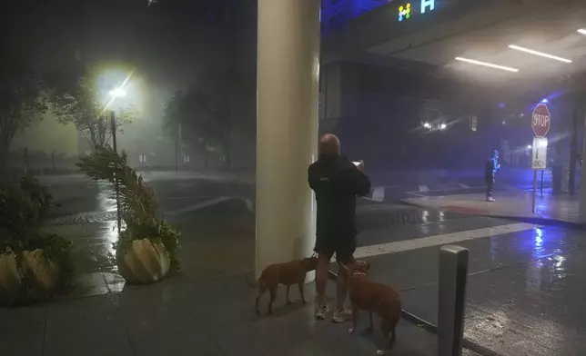 A man walking his dogs takes a picture from the sheltered entryway of the Hyatt Place Downtown Tampa hotel, as strong gusts of wind from Hurricane Milton blow sheets of rain along the street in Tampa, Fla., Wednesday, Oct. 9, 2024. (AP Photo Rebecca Blackwell)