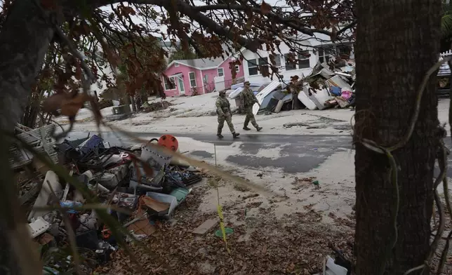 Members of the Florida Army National Guard check for any remaining residents in nearly-deserted Bradenton Beach, where piles of debris from Hurricane Helene still sit outside damaged homes, ahead of the arrival of Hurricane Milton, Tuesday, Oct. 8, 2024, on Anna Maria Island, Fla. (AP Photo/Rebecca Blackwell)