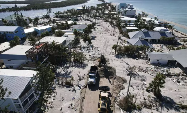 Charlotte County workers clear feet of sand from a road on southern Manasota Key, in Englewood, Fla., following the passage of Hurricane Milton, Sunday, Oct. 13, 2024. (AP Photo/Rebecca Blackwell)